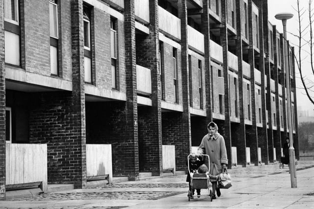 1960:  A woman walking past a block of modern housing with two young children in the Gorbals.