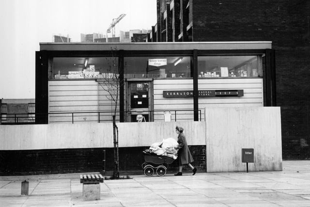 1960:  A woman pushing a pram laden with bedding past a newly built shop in the modern Gorbals.