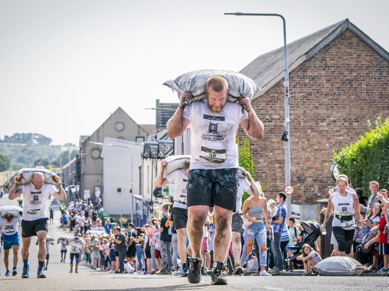 Competitors take part in the Scottish Coal Carrying Championships through the streets of Kelty in Fife. Picture date: Saturday August 28, 2021. PA Photo. The annual event is one of only two Coal Races in the world and the men's race requires participants to carry a 50-kilo bag of coal and the women's race requires a 25-kilo bag of coal to be carried over 1000 metres through the village. Photo credit should read: Jane Barlow/PA Wire