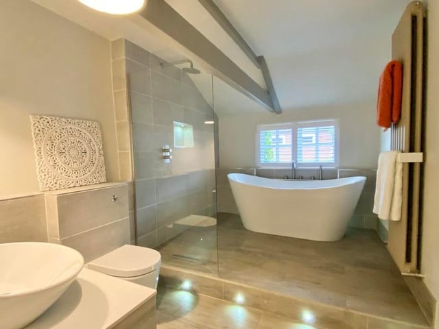 The main bathroom is modern and features not only a double-ended bath with centre tap and shower tap but also a drench shower-head with glass screen. It is topped by a vertical radiator, WC, wash basin with vanity storage beneath, beam ceiling and access to the home's loft.