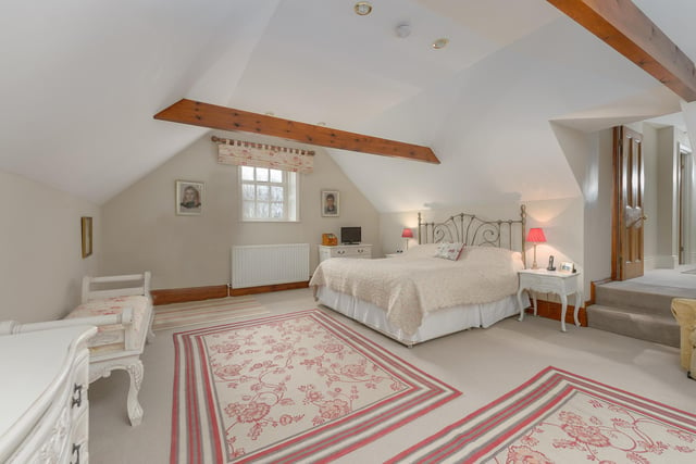 The spacious master bedroom suite with exposed beams leads to a dressing room with fitted furnishing and an en-suite bathroom.