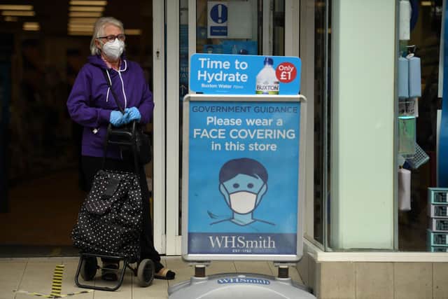 A shopper wearing a face mask stands alongside a sign calling for the wearing of face coverings in shops, in the city centre of Sheffield (Photo by Oli SCARFF / AFP) (Photo by OLI SCARFF/AFP via Getty Images)