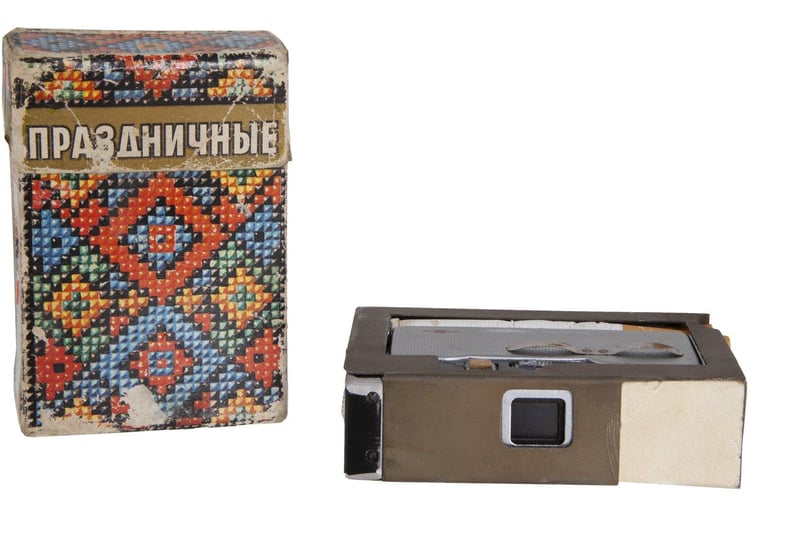 A Soviet KGB spy pack of Holiday brand cigarettes containing a hidden camera, with the lens operating through a small grill on the side. 3 1/2 by 2 1/4 by 1 inches. Estimate: $600-$800.