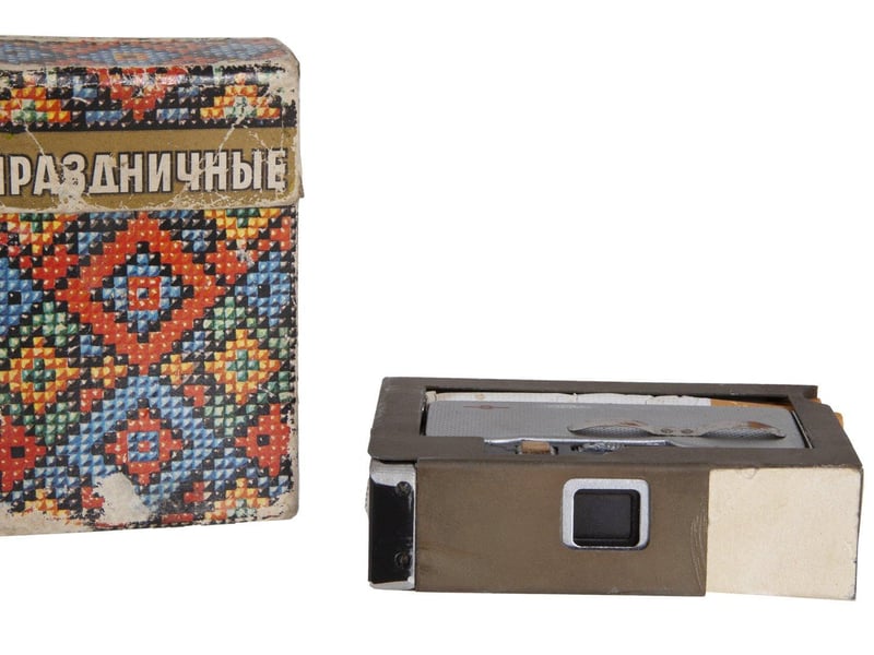 A Soviet KGB spy pack of Holiday brand cigarettes containing a hidden camera, with the lens operating through a small grill on the side. 3 1/2 by 2 1/4 by 1 inches. Estimate: $600-$800.