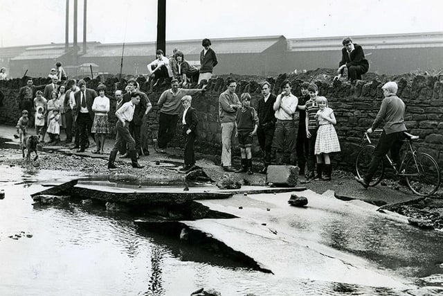 The scene showing the hole in the road and the debris left lying on the road when the water subsided after a burst water main on Brightside Lane, May 30, 1964