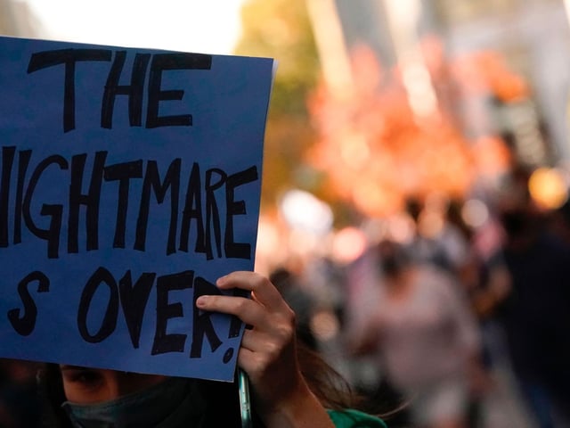 A woman holds a sign reading "The Nightmare is Over" as people celebrate on Black Lives Matter plaza across from the White House in Washington, DC (Photo by ALEX EDELMAN/AFP via Getty Images)