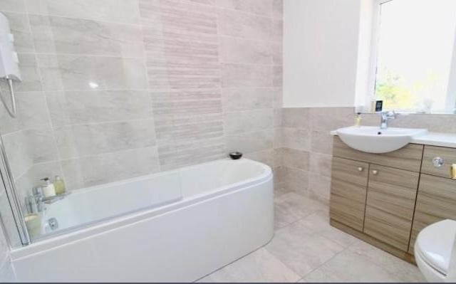 The bathroom is fitted with double glazed window, modern three piece white suite comprising of; oval bath with shower over, low level WC and wash basin in vanity unit, tiled walls, tiled floor and radiator