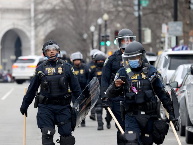 Police officers in riot gear walks towards the U.S. Capitol as protesters enter the building.