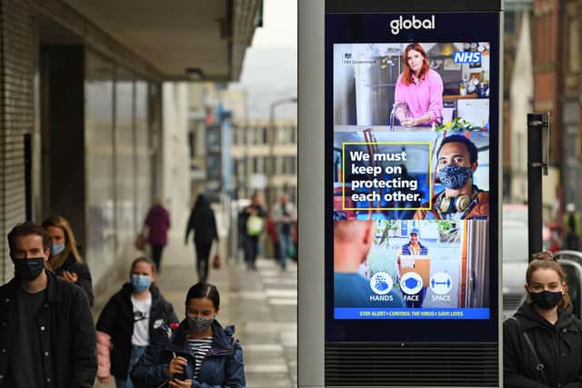 People wearing face masks or coverings due to the Covid-19 pandemic walk past a display featuring health advice in central Sheffield. (Photo by OLI SCARFF/AFP via Getty Images)