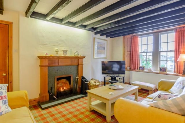 The sitting room, with overhead beams, features an open fireplace, a built-in display cabinet with interior lighting, and a window that connects with an adjoining second sitting room.

Picture: Right Move