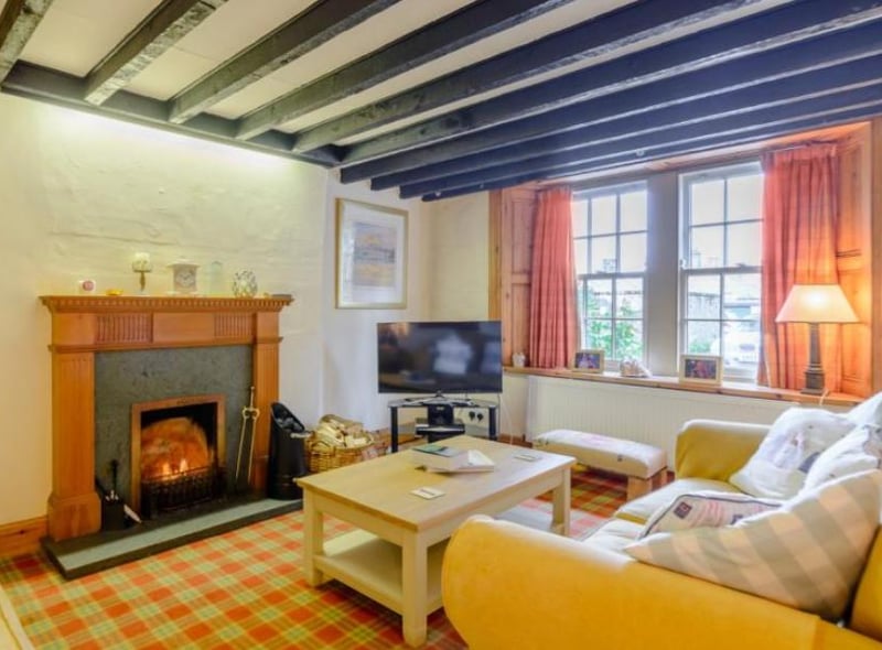 The sitting room, with overhead beams, features an open fireplace, a built-in display cabinet with interior lighting, and a window that connects with an adjoining second sitting room.

Picture: Right Move