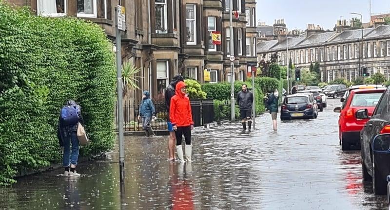 A pedestrian stands in the middle of a flooded street wearing wellies. Severe flash flooding in Stockbridge caused local shops in the area to shut temporarily.