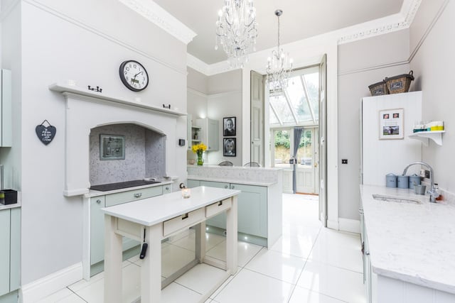 A traditional bespoke kitchen with shaker style base and wall units with quartz surfaces over. Inset sink with mixer tap and drainer, breakfast bar and tiled flooring with underfloor heating.