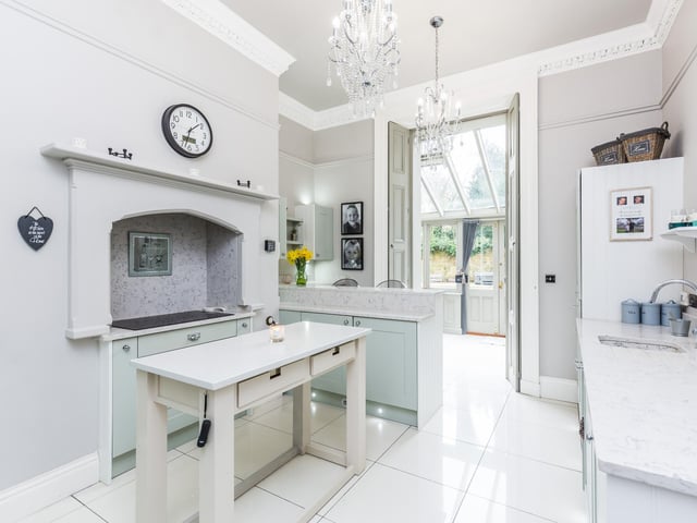 A traditional bespoke kitchen with shaker style base and wall units with quartz surfaces over. Inset sink with mixer tap and drainer, breakfast bar and tiled flooring with underfloor heating.