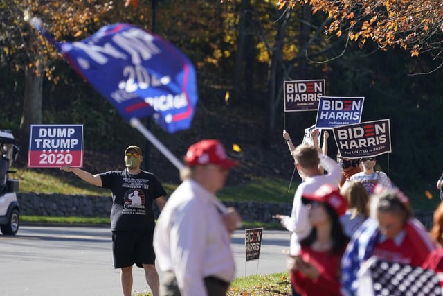 Supporters of President-elect Joe Biden wave signs as Trump supporters wave flags at the entrance to Trump National golf club in Sterling, Va. (AP Photo/Steve Helber)