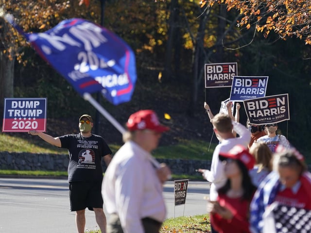 Supporters of President-elect Joe Biden wave signs as Trump supporters wave flags at the entrance to Trump National golf club in Sterling, Va. (AP Photo/Steve Helber)