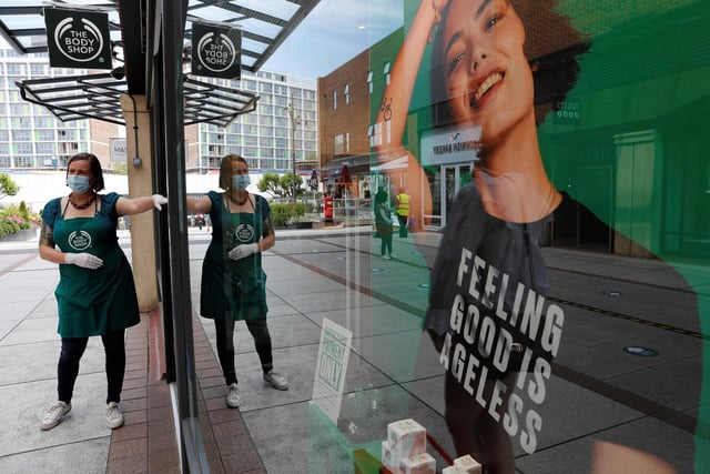 A retail worker wearing PPE (personal protective equipment), of gloves and a face mask or covering as a precautionary measure against COVID-19, directs customers waiting to enter a The Body Shop cosmetics store
