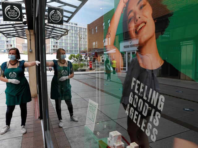 A retail worker wearing PPE (personal protective equipment), of gloves and a face mask or covering as a precautionary measure against COVID-19, directs customers waiting to enter a The Body Shop cosmetics store