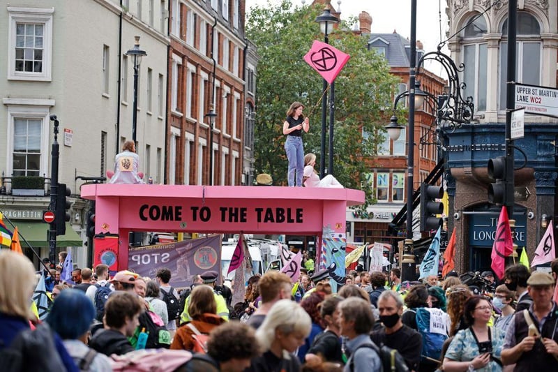 Climate activists from the Extinction Rebellion sit and stand atop their large pink table they set up in a road in central London (Photo by TOLGA AKMEN/AFP via Getty Images)