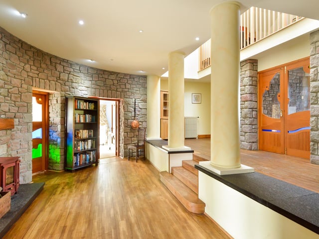 The front door opens to a split-level semicircular hallway with a central fireplace and glazed doors leading to all the ground-floor reception rooms