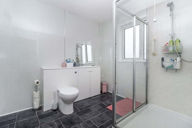 The generous family shower room has wet wall panelling and features a walk-in shower with glazed enclosure, WC, and wash hand basin within a vanity unit.