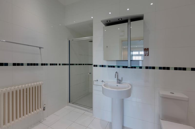 The ensuite for bedroom four boasts a white suite comprising a low-level WC and pedestal wash hand basin with a mirrored vanity unit above. To one corner, there is a separate shower enclosure.