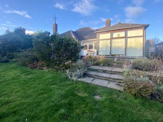 This is a view of the back of the bungalow from its garden. A paved patio area has some steps that lead on to a lawn.