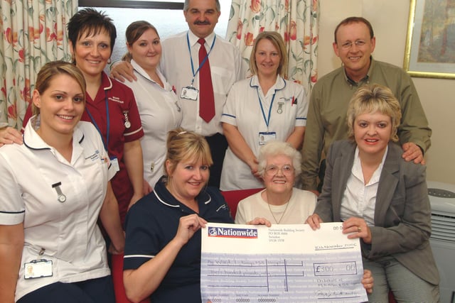 Mary Allen, seated right, presented a cheque for £300 in lieu of flowers in memory of her husband Geoffrey Allen assisted by her daughter and son-in-law Sarah and Russell Currins, right, to Ward 7 at Kings Mill Hospital in 2006. Ward Leader Jane Tomlinson, seated left, receives the cheque watched by staff members from the left; Holly Kime Staff Nurse, Bev Pickering Ward Housekeeper, Jenni Currie Staff Nurse, Eric Adams Ward Receptionist and Kerry Mason Assistant Nurse Practitioner.