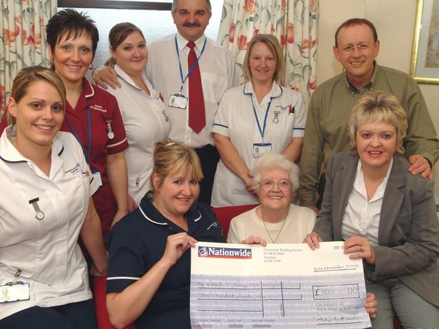 Mary Allen, seated right, presented a cheque for £300 in lieu of flowers in memory of her husband Geoffrey Allen assisted by her daughter and son-in-law Sarah and Russell Currins, right, to Ward 7 at Kings Mill Hospital in 2006. Ward Leader Jane Tomlinson, seated left, receives the cheque watched by staff members from the left; Holly Kime Staff Nurse, Bev Pickering Ward Housekeeper, Jenni Currie Staff Nurse, Eric Adams Ward Receptionist and Kerry Mason Assistant Nurse Practitioner.