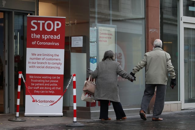A couple walk past a coronavirus advice sign outside a bank on Argyle Street in Glasgow city centre the morning after stricter lockdown measures came into force