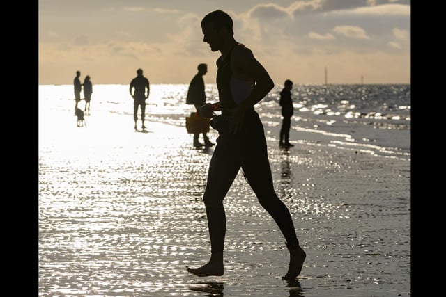 A triathlete is silhouetted against the sky as he emerges from the sea taken by Keith Woodland