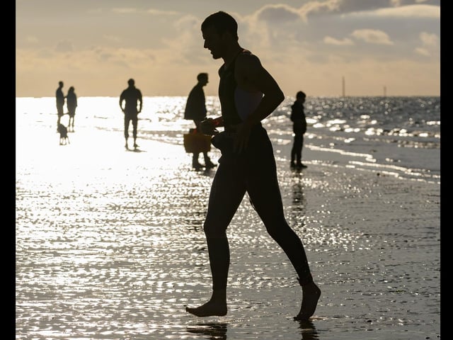 A triathlete is silhouetted against the sky as he emerges from the sea taken by Keith Woodland