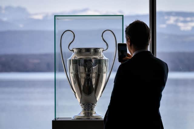 A man takes a picture of the UEFA Champions League trophy displayed at the UEFA headquarters: FABRICE COFFRINI/AFP via Getty Images