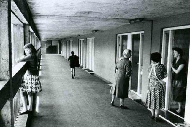 A young girl peers out from one of the Upper floor deck walkways connecting some of the Park Hill Estate high rise flats (Park Hill I) in Sheffield, England while a group of housewives chat on a doorstep - April, 1961. Roger Mayne Archive / Mary Evans Picture Library