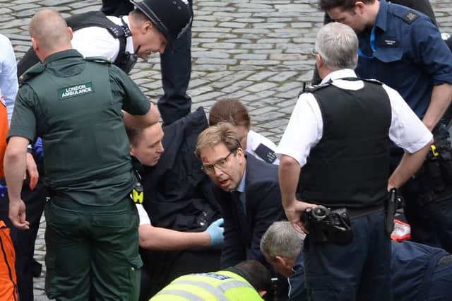 Conservative MP Tobias Ellwood (centre) helps emergency services attend to a police officer outside the Palace of Westminster