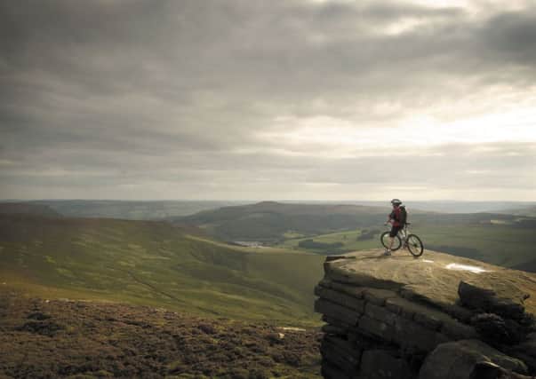 A lone cyclist taking in the spectacular view of the Peak District from the top of Whinstone Lee Tor