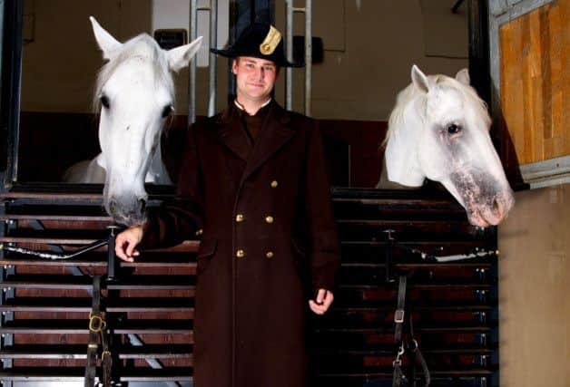 Rider Florean Bacher from The Spanish Riding School of Vienna poses with two Lipizzaner stallions  as they peer out if their stables at Austrian capital's Imperial Palace.