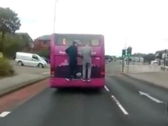 The men pictured hanging onto the back of a moving bus in Sheffield. (Photo: YouTube).