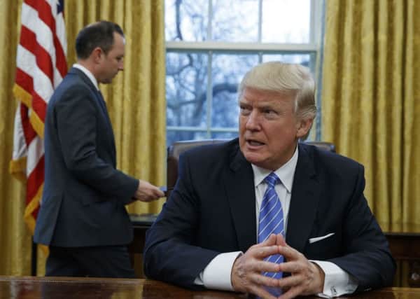 President Donald Trump sits at his desk as he waits for White House Chief of Staff Reince Priebus, left, to deliver three executive orders for his signature, Monday, Jan. 23, 2017, in the Oval Office of the White House in Washington. (AP Photo/Evan Vucci)
