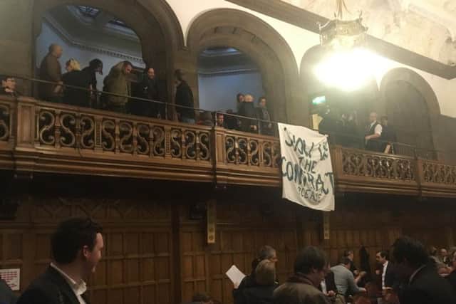 Protesters unfurl a banner within the council chamber